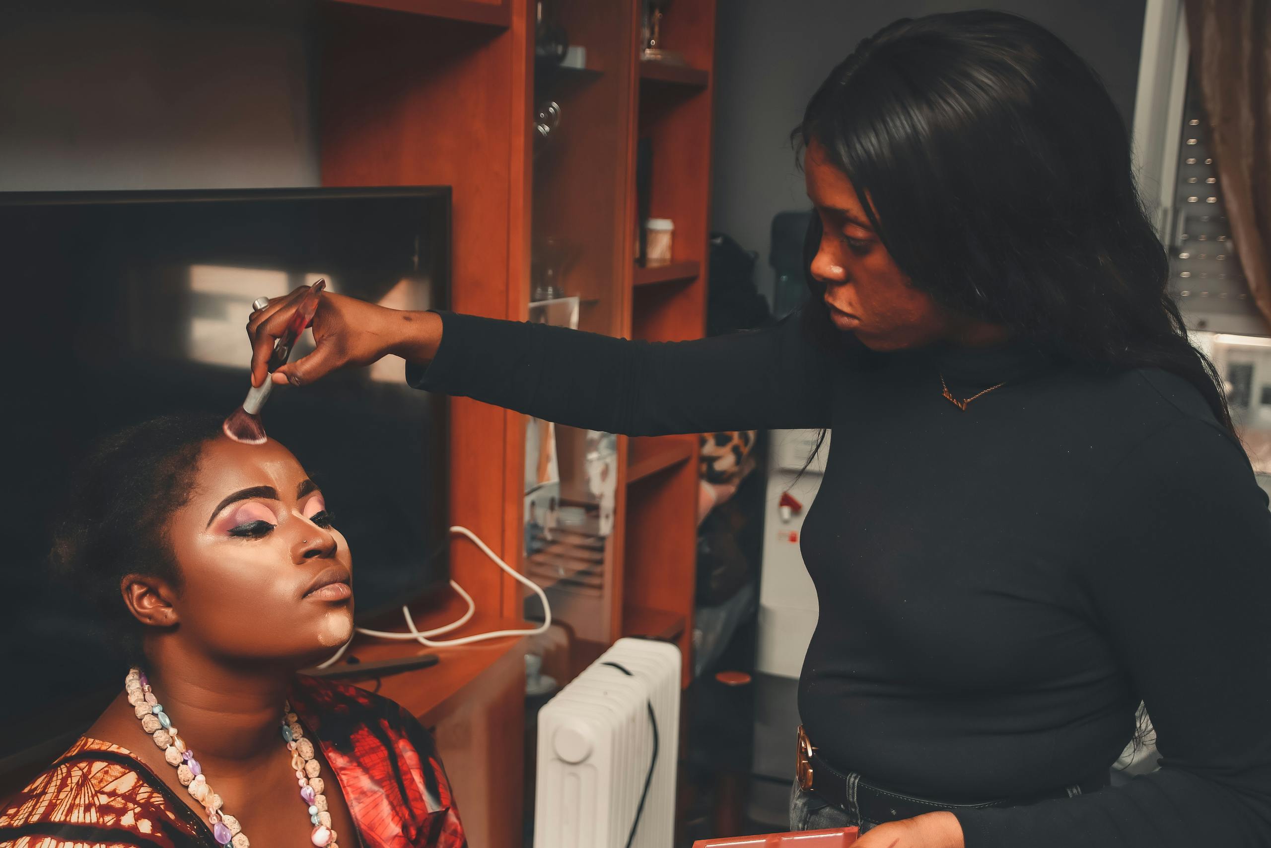 A makeup artist skillfully applies makeup to a woman, enhancing her beauty indoors.