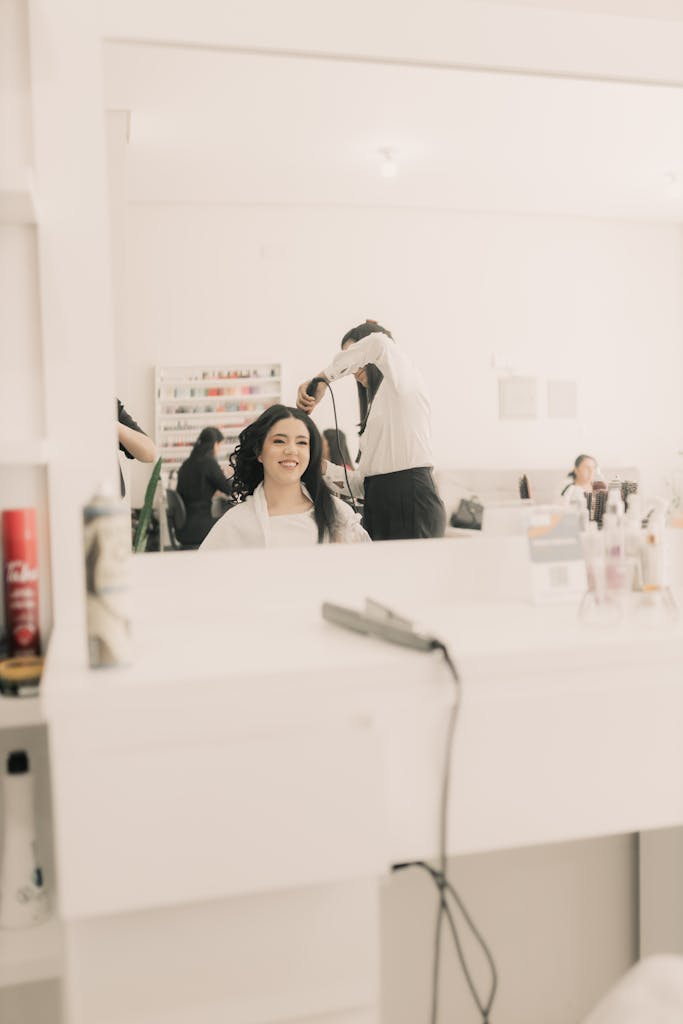 Woman having her hair styled in a bright, modern salon with a smiling reflection in the mirror.